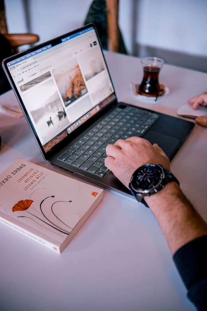 Close-up of a person working on a laptop with a watch, book, and coffee cup.